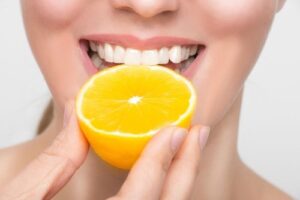 Mujer sonriendo con una media naranja por comer en la mano